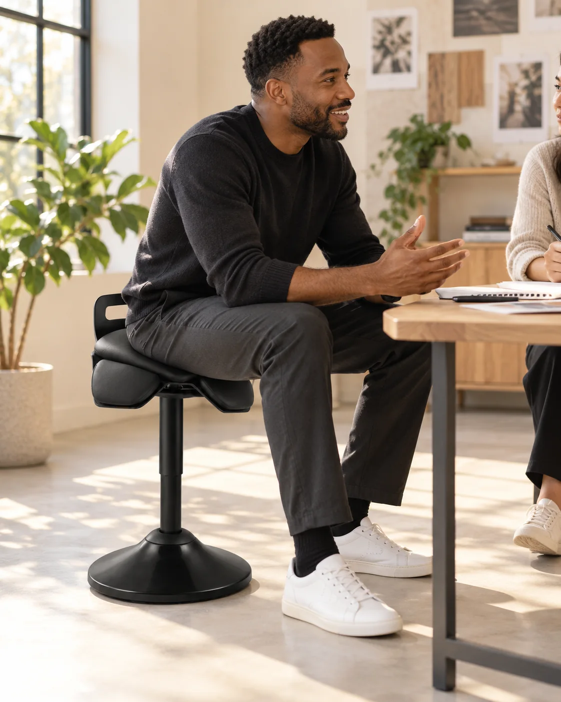 Man using a black three-part wobble stool in a bright workspace