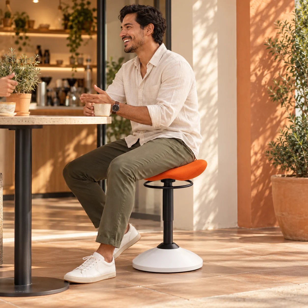 Man sitting on the orange Saddle stool in a sunny café
